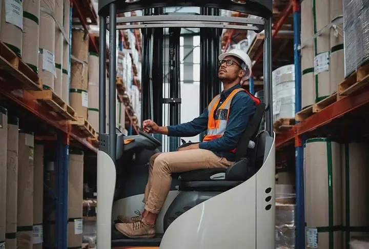 A man in safety vest driving a forklift.